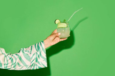 Yeşil arka planda ipotekli ve salatalık tadında ferahlatıcı tatlı ve ekşi bir kokteyli olan kadın el ele tutuşuyor. Alkol ve alkolsüz içki, parti, tatil kavramı. İlan için alanı kopyala