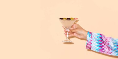 Kadın, arka planda yeşil zeytinli martini bardağı tutuyor. Alkol ve alkolsüz içecek kavramı, parti, tatil, bar, karışım. Poster. İlan için alanı kopyala