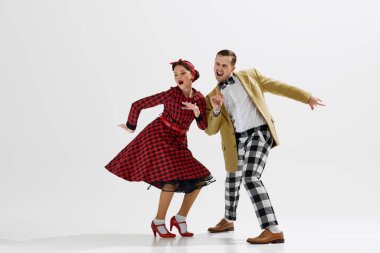 Kareli pantolonlu ve hardal ceketli bir adam beyaz stüdyo arka planında dans eden kırmızı ekose elbiseli bir kadınla dans ediyor. Sanat anlayışı, retro ve vintage, hobi, eğlence, 20 'ler