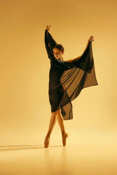 受到电影的启发 优雅的年轻女子 有着金色脸庞的芭蕾舞演员 穿着黑色服装 站在黄底尖上 艺术概念 古典舞蹈 — 图库照片#
