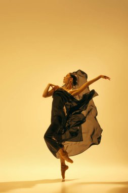 Yaratıcı bir performans sergileyen, kum rengi arka planda akan siyah kostüm içinde dans eden uzun boylu, güzel bir bayan balerin. Sanat kavramı, klasik dans, güzellik, moda, estetik