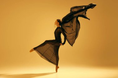 Dinamik bale hareketi. Sanatsal bayan balerin, siyah akış elbiseli balerin sarı arka planda dans ediyor. Sanat anlayışı, klasik dans, güzellik ve moda