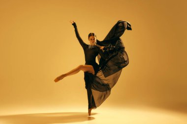 Sanatsal ve anlamlı bir performans. Genç bir kadın, siyah giyinmiş balerin altın arka planda dans ediyor. Sanat kavramı, klasik dans, güzellik ve moda, estetik.
