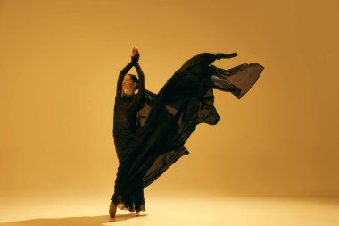 Özgürlük ve ilham. Genç bayan balerin siyah akıcı kostüm giyiyor ve kum rengi arka planda dans ediyor. Sanat kavramı, klasik dans, güzellik ve moda, estetik.