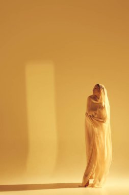 Şefkat ve zarafet. Açık renk kumaşlı güzel bir kadın, kumlu arka planda dans eden bir balerin. Sanat kavramı, klasik dans, güzellik ve moda, estetik.