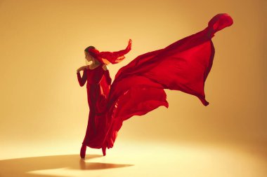 Zarafet ve tutku. Kırmızı akıcı elbise giyen ve kum rengi arka planda performans sergileyen bir kadın sanatçı. Sanat kavramı, klasik dans, güzellik ve moda, estetik.