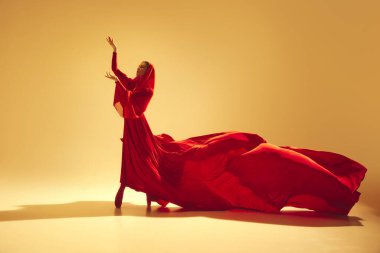 Tutku harekete geçti. Güzel bir kadın, akıcı kırmızı elbiseli bir dansçı kum rengi arka planda güçlü bir performans sergiliyor. Sanat kavramı, klasik dans, güzellik ve moda, estetik.