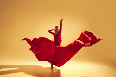 Sanatsal ve derin performanslı kadın, akıcı kırmızı elbiseli kadın dansçı, altın renkli arka planda dans ediyor. Sanat kavramı, klasik dans, güzellik ve moda, estetik.