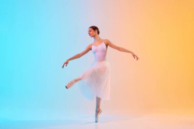 Beyaz etekli genç balerin mavi-turuncu arka plana karşı neon ışıkta dans figürleri deniyor. Sanat, hareket, klasik ve modern birleşme, güzellik ve moda kavramı. Ad