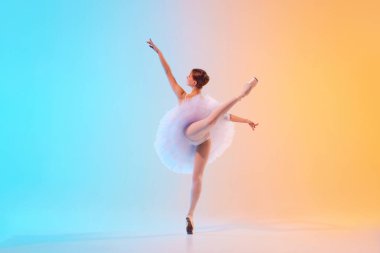 Beyaz etekli genç balerinin mavi-turuncu gradyan arkaplana karşı neon ışıkta arabesk hareketini arka planda izlemesi. Sanat, hareket, klasik ve modern birleşme, güzellik, moda kavramı. Ad