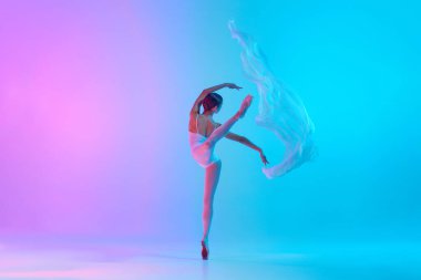 Zarif bale sanatçısı beyaz kumaşla canlı gradyan arkaplana karşı neon ışığı altında gösteri yapıyor. Sanat, hareket, klasik ve modern birleşme, güzellik ve moda kavramı. Ad