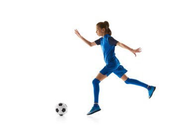 Hareket halindeki bir genç, mavi üniformalı bir kız top sürüyor, beyaz stüdyo arka planında izole edilmiş futbol becerileri üzerinde çalışıyor. Spor anlayışı, aktif ve sağlıklı yaşam tarzı, çocukluk, okul, hobi