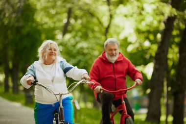 Sürüş etkinliği. Yaşlı çift, güneşli sıcak bir günde parkta bisiklet süren erkek ve kadın, rahatlatıcı spor aktiviteleri gösteriyorlar. Spor anlayışı, yaşlanma, aktif ve sağlıklı yaşam tarzı, sağlık hizmetleri