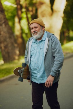 Kaykaylı yaşlı bir adamın portresi, genç hobi aşığı yemyeşil parkın arka planında yürüyor. Spor anlayışı, yaşlanma, aktif ve sağlıklı yaşam tarzı, sağlık hizmetleri