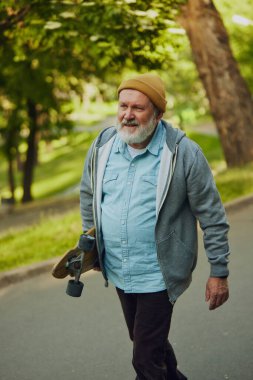 Kaykaylı yaşlı bir adamın portresi, genç hobi aşığı yemyeşil parkın arka planında yürüyor. Spor anlayışı, yaşlanma, aktif ve sağlıklı yaşam tarzı, sağlık hizmetleri