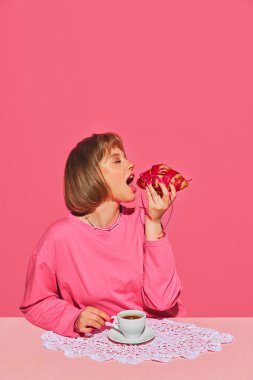Güzel, genç, sarışın kız pembe arka planda gözleri kapalı, taze pişmiş kruvasanın tadını çıkarıyor. Yaratıcı fotoğrafçılık kavramı, pop sanat tarzı, hayal gücü.