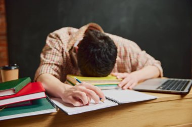 Uzun saatler çalıştıktan sonra yorgun hissediyorum. Genç bir çocuk, sınıfta kafası masanın üstünde, elleri notların üzerinde oturuyor. Yorgunluk ifadesi. Eğitim, öğrenim, ödev, yaşam tarzı kavramı