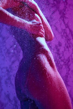 Kadın vücudu, bacakları ve kalçaları su damlalarının altında kesilmiş. Kadın neon ışıkta rahatlatıcı bir duş alıyor. Güzellik, kaplıca, rahatlama, banyo kozmetik ürünleri, sağlık.