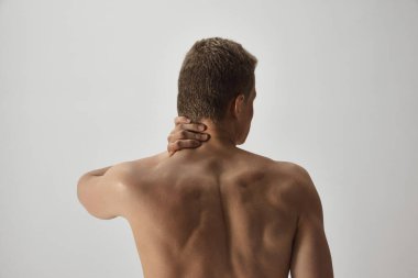 Boynunu tutan, omurgadan muzdarip, gri stüdyo arka planında izole edilmiş boynu ağrılı bir adamın dikiz görüntüsü. Erkek güzelliği, vücut bakımı, spor, sağlık, tıbbi bakım kavramı
