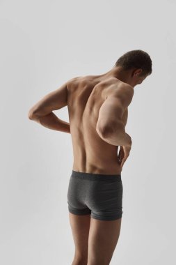 Gri stüdyo arka planında izole edilmiş külotlu çorap giymiş, sarı saçlı genç adam. Mükemmel kaslı vücut şekli. Arkadan bak. Erkek güzelliği, vücut bakımı, spor, sağlık