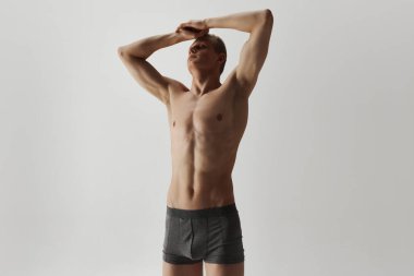 Erkek iç çamaşırı koleksiyonu ve... Gri pamuklu boksörlerle poz veren kaslı vücutlu yakışıklı genç adam gri stüdyo arka planında izole edilmiş. Erkek güzelliği, vücut bakımı, spor, sağlık