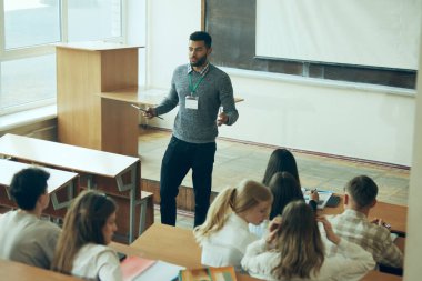 Etkileşimli Öğrenme Oturumu. Sınıfın önünde ders veren genç öğretmen, çeşitli öğrenci gruplarıyla ilgileniyor. Modern öğretim yöntemleri. Eğitim kavramı, gençlik, atölye, bilgi