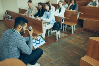 İş ve analitik dersi. Üniversite sınıfında oturan bir grup genç ve çok ırklı öğrenciye ders veren genç öğretmen. Eğitim kavramı, gençlik, atölye, bilgi