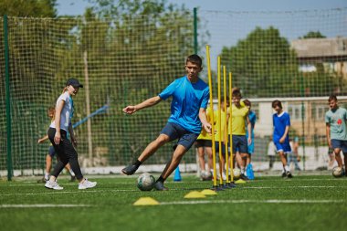 Takım çalışması ve çeviklik. Futbol sahasında formalı genç futbolcular antrenörleriyle birlikte açık havada yağmur yağıyor. Yetenekleri ve dayanıklılıkları artıyor. Spor, okul, çocukluk, hobi, aktif yaşam tarzı kavramı