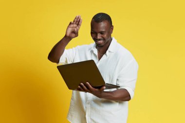 Mutlu gülümseyen Afro-Amerikalı adam, arkadaşları ve meslektaşlarıyla çevrimiçi video görüşmesi için bilgisayarını kullanıyor. İnsan duyguları kavramı yüz ifadesi, moda
