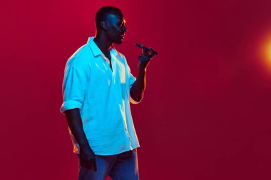 Afro-Amerikalı bir adam şık günlük kıyafet tarzında cep telefonuyla sesli mesaj kaydediyor, kırmızı arka planda neon ışıkta konuşuyor. İnsan duyguları kavramı yüz ifadesi, moda