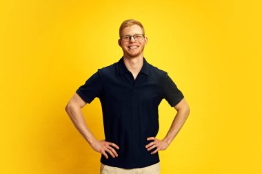 Gözlüklü, siyah gömlekli, kendine güvenen ve parlak sarı arka planda gülümseyen genç bir kızıl adam portresi. İnsan duyguları, yüz ifadesi, yaşam tarzı kavramı