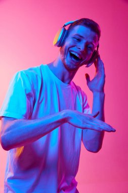 DJ 'lik. Beyaz tişörtlü genç bir adamın portresi kulaklıkla müzik dinliyor, neon ışıkta pembe arka planda şarkı söylüyor ve eğleniyor. İnsan duyguları, yüz ifadesi, yaşam tarzı kavramı