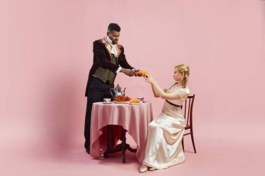 Ortak kahvaltı. Rönesans kıyafetleri içinde yakışıklı bir adam ve zayıf bir kadın. Pembe arka planda kahvaltıda böğürtlen ve kruvasan yiyor. Tarih kavramı, retro ve vintage, çağların karşılaştırması