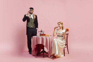 Vikont ve Vikont. Dönem kostümlü kadın ve erkek. Pembe stüdyo geçmişine karşı. Cep telefonuyla konuşan bir adam, kruvasan yiyen bir kadın. Tarih, retro ve vintage, dönemin karşılaştırması