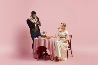 Tech Twist 'le Tarihi Kahvaltı. Pembe stüdyo arka planında zarif genç bir kadının telefonuyla fotoğraf çeken bir adam. Tarih kavramı, retro ve vintage, çağların karşılaştırması