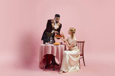 Edwardian döneminin zarafeti. Dönem kıyafetli bir adam pembe arka planda kadınlara çilek servis ediyor. Üst sınıf hayatın boş ve lüks ortamları. Tarih, retro ve vintage, dönemin karşılaştırması