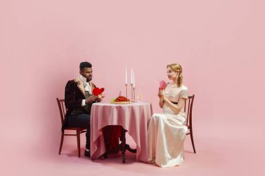 Rönesans kıyafetli bir çiftin tarihi sahnesi, flörtleşmenin keyfi, pembe arka planda aşkı simgeleyen kalpleri paylaşmak. Tarih kavramı, retro ve vintage, çağların karşılaştırması