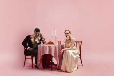 Şık bir adam bir kadın, kraliyet mensupları 3 boyutlu gözlüklerle masada oturuyor ve pembe stüdyo arka planında film izliyor. - Boş zaman. Tarih kavramı, retro ve vintage, çağların karşılaştırması