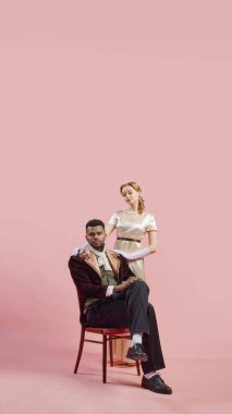 Barok zarafeti. Barok esinlenilmiş kadife ceketli bir adam pembe stüdyo arka planında yanında duran zarif bir kadınla oturuyor. Tarih kavramı, retro ve vintage, çağların karşılaştırması