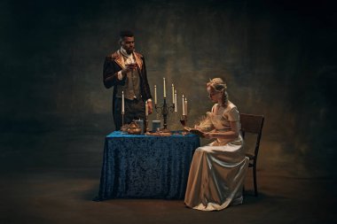 Klasik giysili zarif bir adam masanın yanında mum taşıyan bir şarap kadehi tutuyor, saten elbise giyen bir kadın kitap okuyor. Az aydınlatılmış, tarihi bir geçmiş. Tarih, retro ve vintage, dönemin karşılaştırması