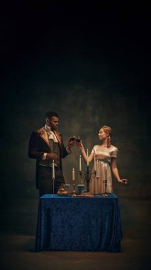 Şık giyinmiş, mum ışığında şarap içen, karanlık ve dengesiz bir çift. Romantik bir akşam. Tarih kavramı, retro ve vintage, çağların karşılaştırması