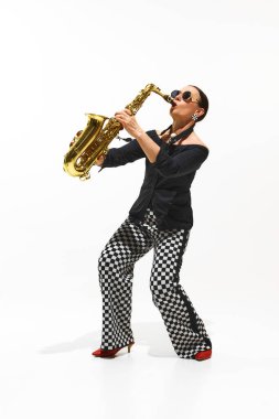 Zarif bir kadın, kareli pantolonlu bir müzisyen beyaz arka planda saksafon çalıyor. Müzik, festival, konser, hobi, yetenek, performans kavramı