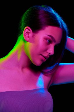 Zenginlik ve çekicilik, bakımlı cildi ve saçı siyah stüdyonun arka planında neon ışığında poz veren zarif genç kız. Doğal güzellik kavramı, cilt bakımı, gençlik, sağlık.