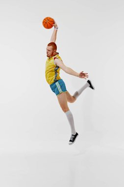 Gecekondu baskını. Sarı formalı ve mavi şortlu genç bir adamın tam boy görüntüsü, beyaz arka planda topu olan hareketli bir basketbolcu. Spor anlayışı, retro tarzı, aktif yaşam tarzı, hobi