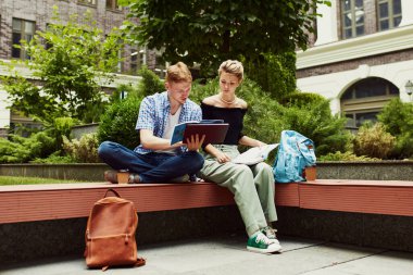 Genel proje hazırlığı. Genç bir adam ve kız, dışarıda sahilde oturan ve birlikte ders çalışan öğrenciler. Sıcak bir sonbahar günü. Eğitim kavramı, üniversite, gençlik, gelecek, arkadaşlık