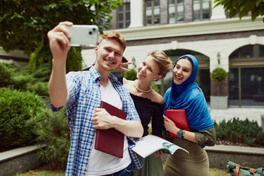 Mutlu gülümseyen öğrenciler, erkek ve kızlar üniversite kampüsünde selfie çekiyorlar. Eğitim sezonuna başlıyoruz. Arkadaşlık. Eğitim kavramı, üniversite, çok kültürlü öğrenciler, birlik