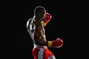 Aparkat yumruğu. Güçlü vücutlu kararlı kaslı bir adam, hareketli bir boks atleti, siyah arka planda izole edilmiş bir şekilde dövüşüyor. Profesyonel spor anlayışı, aktif yaşam tarzı, vücut, güç