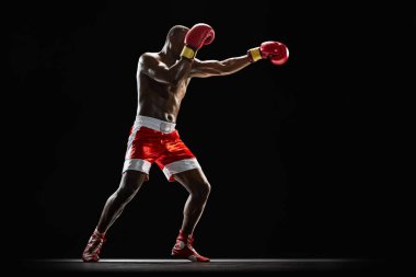 Kırmızı ve beyaz boks şortlu kendine güvenen sporcu, bir sonraki raunda hazırlanıyor, siyah arka planda izole edilmiş antrenman. Profesyonel spor anlayışı, aktif yaşam tarzı, vücut, güç