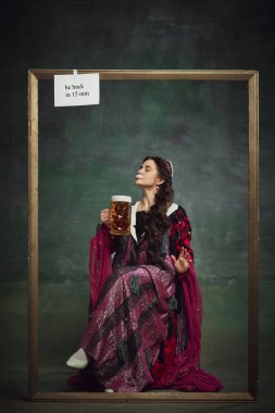 Zarif genç bir kadın, asil bir insan köpüklü bira içiyor ve klasik yeşil arka plandan zevk alıyor. Bira fabrikası, bar. Tarih kavramı, çağların karşılaştırması, yeniden yapım