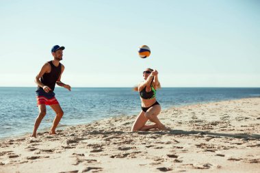 Plaj voleybolu maçında iki oyuncu, hareketli erkek ve kadın, arka planda denizle oynuyor, ve parlak yaz gökyüzü. Spor anlayışı, yaz, doğa, aktif yaşam tarzı, gençlik